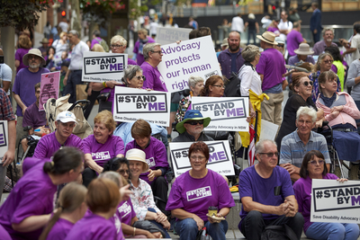 Image of people protesting in purple shirts with placcards