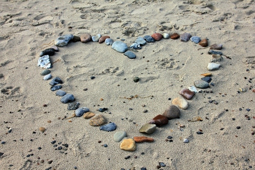 A heart made of stones is laid out on a sandy beach