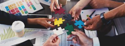 A diverse group of people holding different coloured puzzle pieces in a circle,