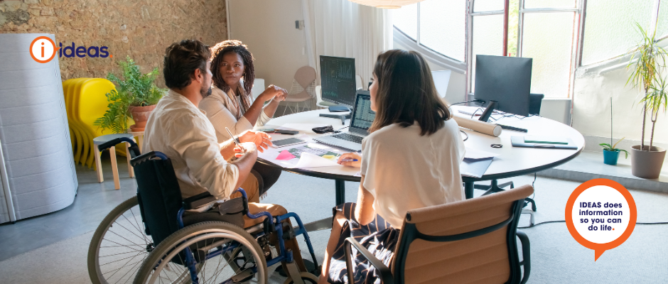A wheelchair user and 2 other people siting at a table discussing work..