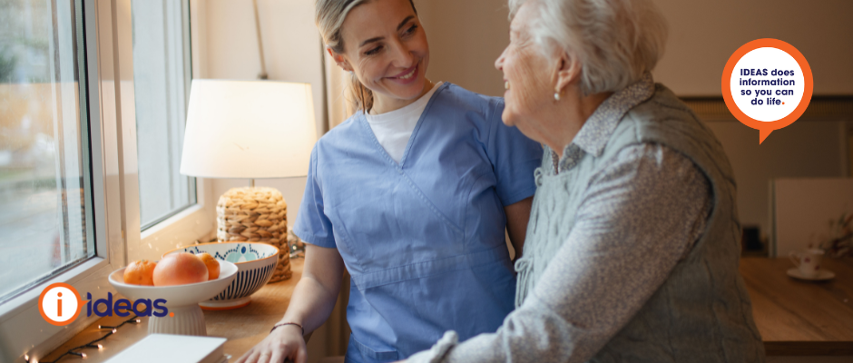 Image of an elderly person and a carer, standing at a kitchen bench.