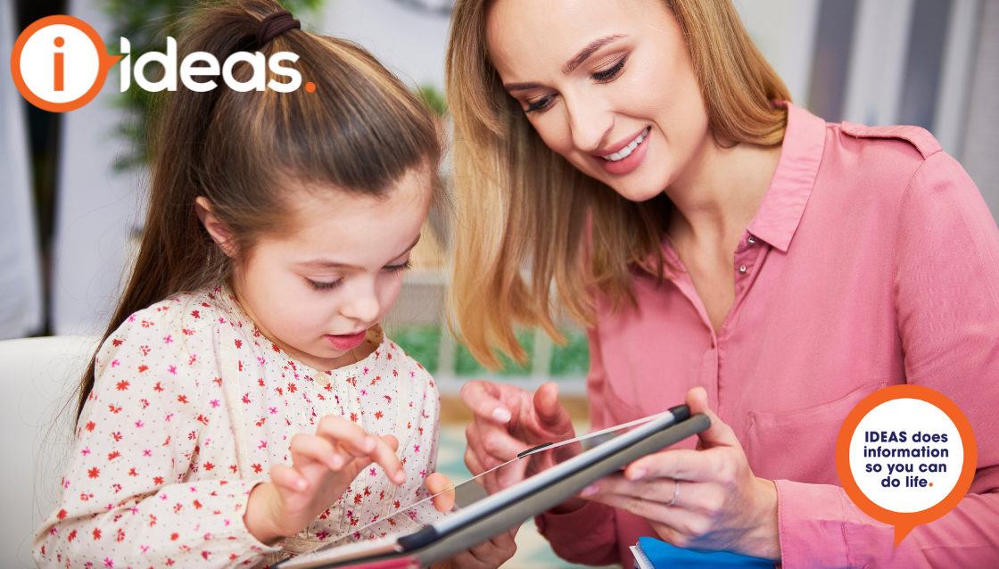 Mother helps a female toddler use an ipad.