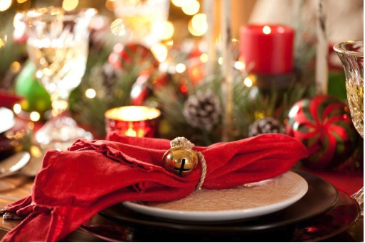 Table set in Christmas decorations and candles. The plates on the tables have a red napkin with a bell tied around the napkin 