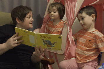 A parent is reading a book to 2 children who wear matching t-shirts