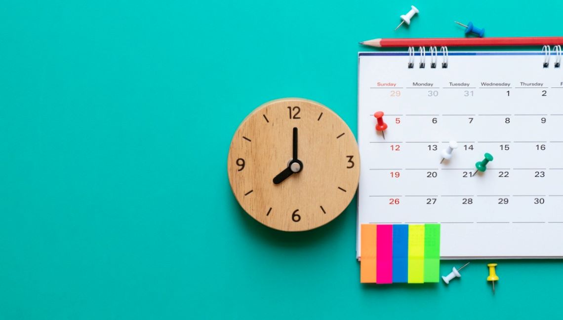 AA close up a wooden clock and a calendar with pins and post-it notes