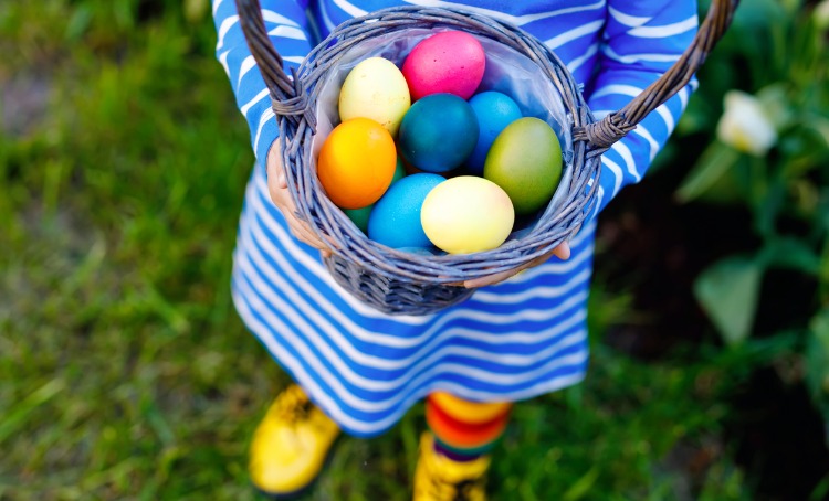 A child is holding a basket filled with colourful Easter eggs.