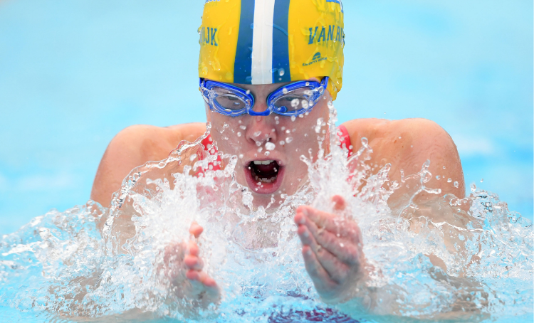 Young woman swimming Breastroke with yellow, blue and white swimming cap and purple goggles. 