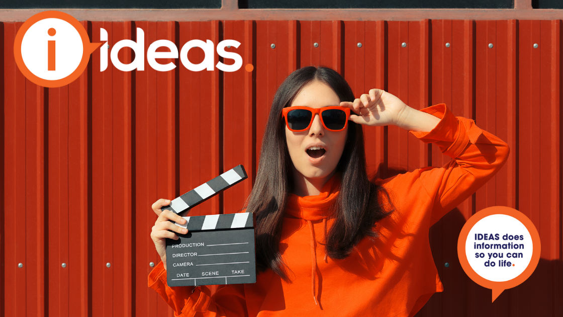 woman with orange sunglasses standing in front of an orange backdrop. She is holding a clapperboard.