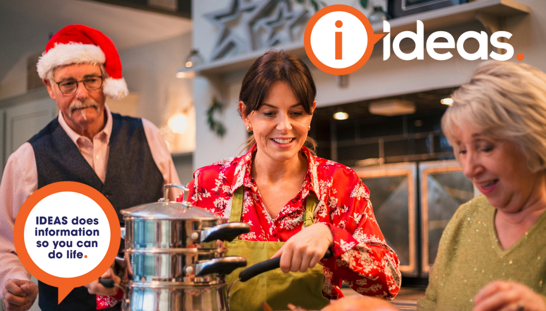 3 people standing in kitchen cooking a christmas meal, with one male wearing a santa hat.