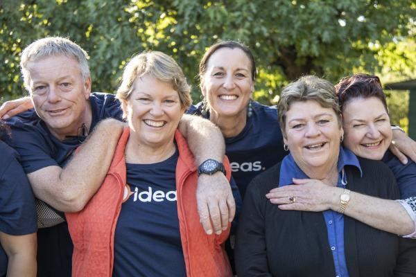 four women and a man in ideas uniforms smiling and hugging each other. 