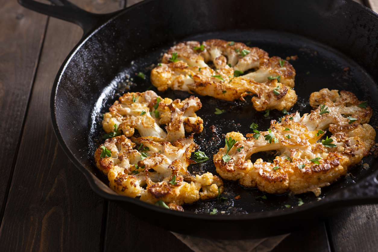 thiuck slices of fried cauliflower in a cast iron skillet