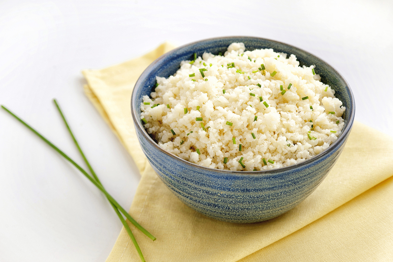 a blue bowl and a yellow cloth filled with cauliflower 'rice' and sprinkled with chives. 