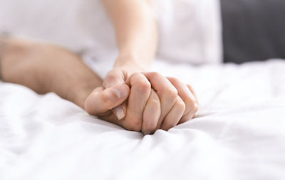 detail of couple's hands clasped tightly on a bed