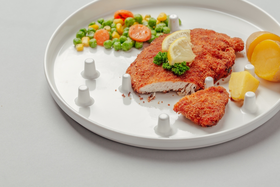 a white plate with crumbed chicken, peas and carrots and corn. the plate has white pegs and slight gradient.