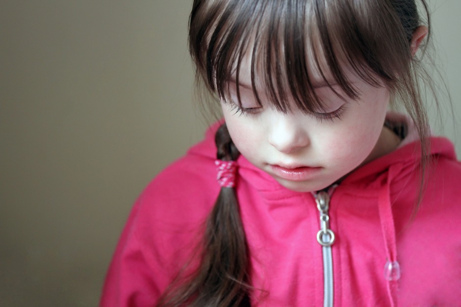 Image of young girl with Down Syndrome looking sad