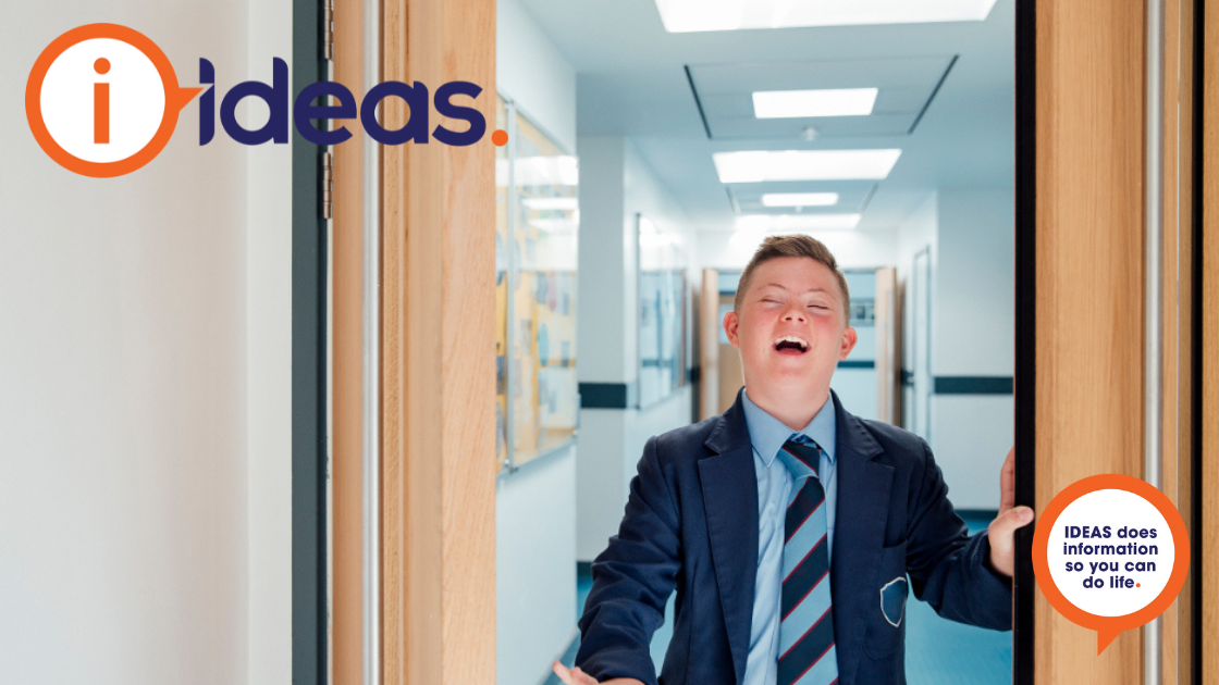 A boy in school uniform is walking though a corridor smiling.