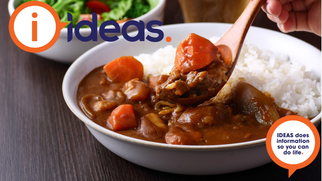 A person is holding a wooden spoon above a A white bowl with boiled rice and Japanese curry of vegetables and meat. 