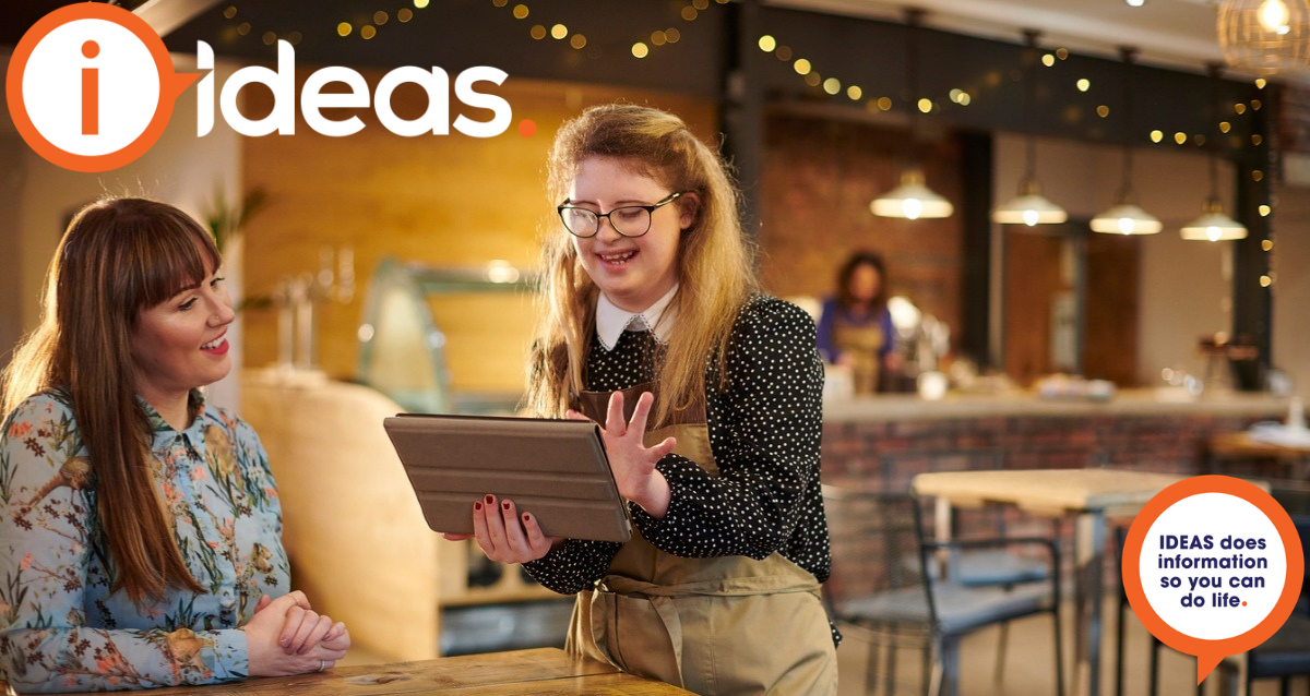 Two women in a coffee shop. One with disability is using a device to take the customers order.