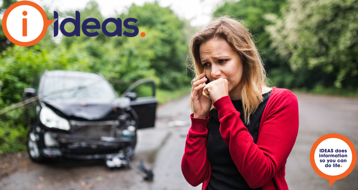 A woman with a worried look on her face and hand clenched to her jaw is calling someone on a smartphone. Behind her is a damaged car.