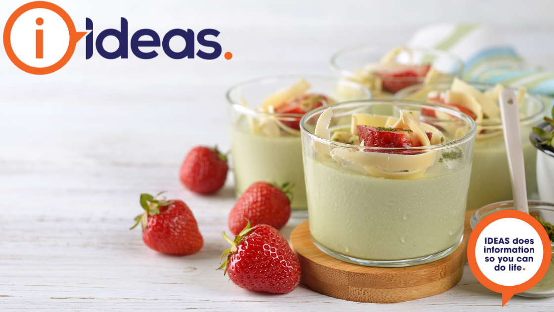 Clear glasses with a pale green panna cotta dessert, are topped with strawberries and white chocolate shavings.
