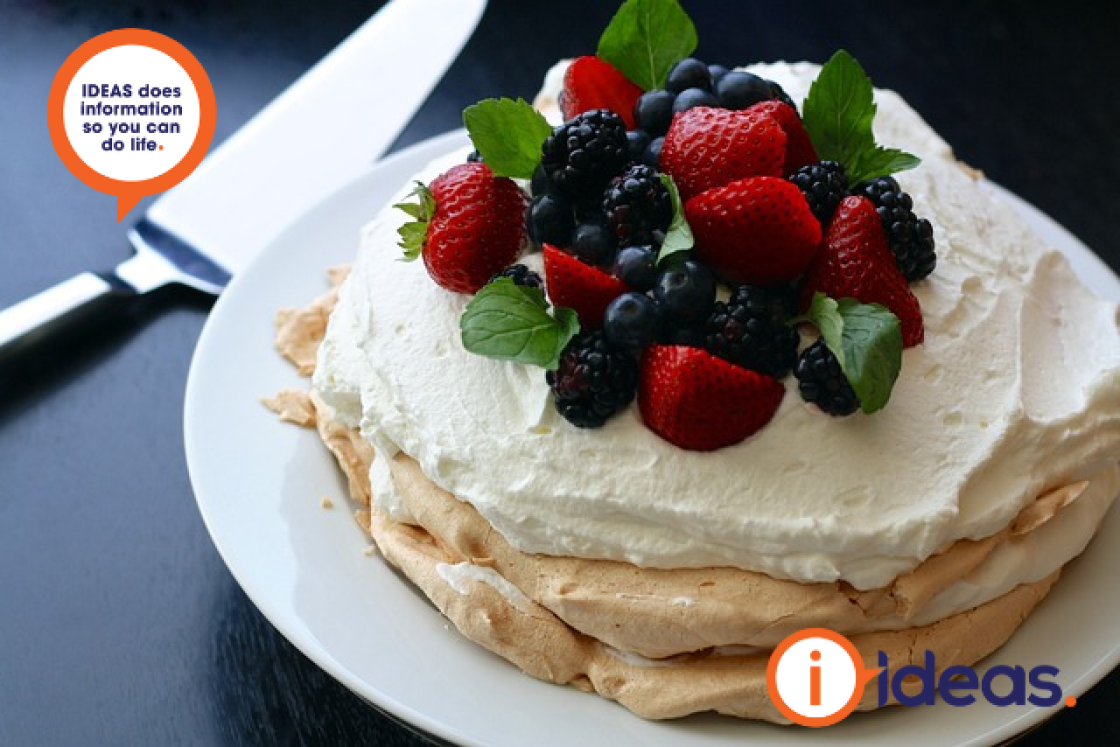 Pavlova dessert that has cream and mixed berries on top, sitting on a plate with a serving knife on the left.