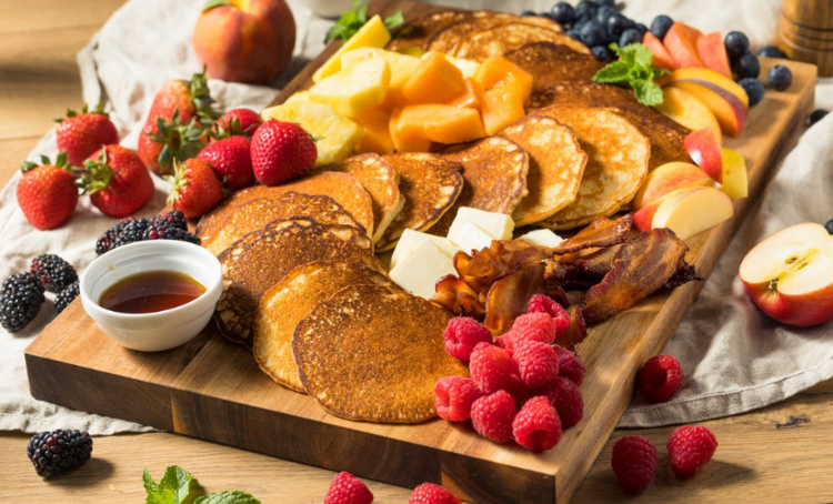 Pancake board with berries, sauces, fruit, butter, bacon