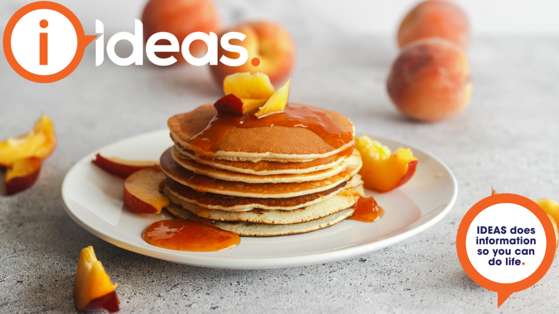 A pancake stack on a plate with apricot jam drizzled and peaches.