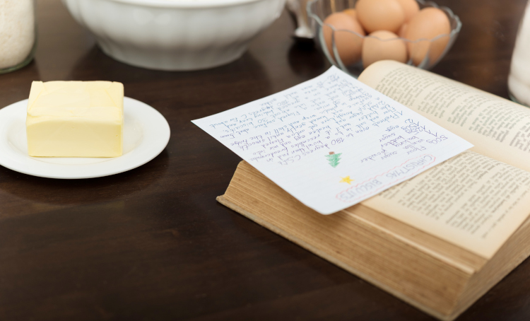 Recipe Book, with a handwritten recipe resting on it. To the side are butter and eggs.