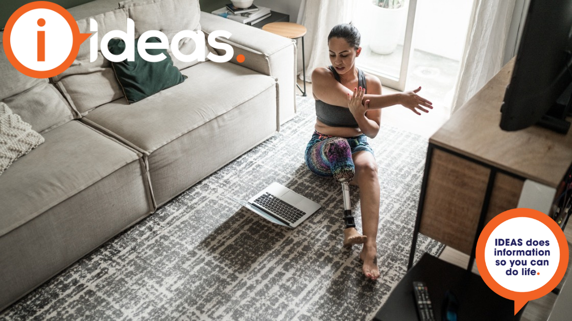 Woman with prosthetic leg sit on the floor in front of a laptop and stretches