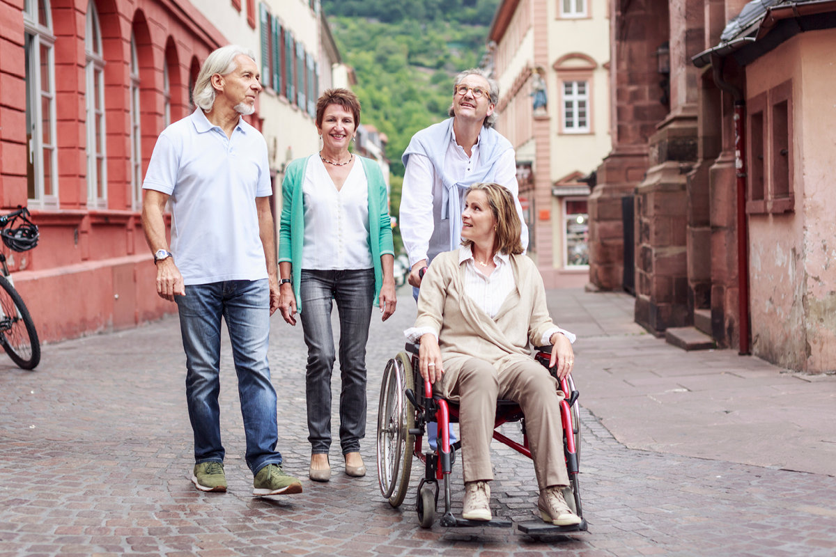 friends moving down a cobbled street. One person is a wheelchair user. All are smiling and talking.