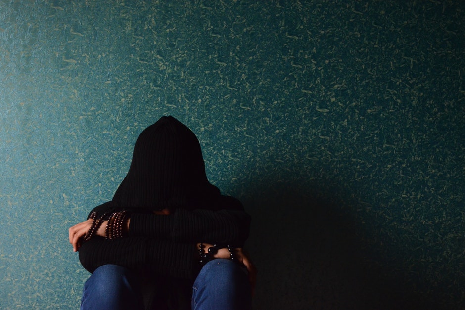 Person sitting with back against wall with a black blanket over head