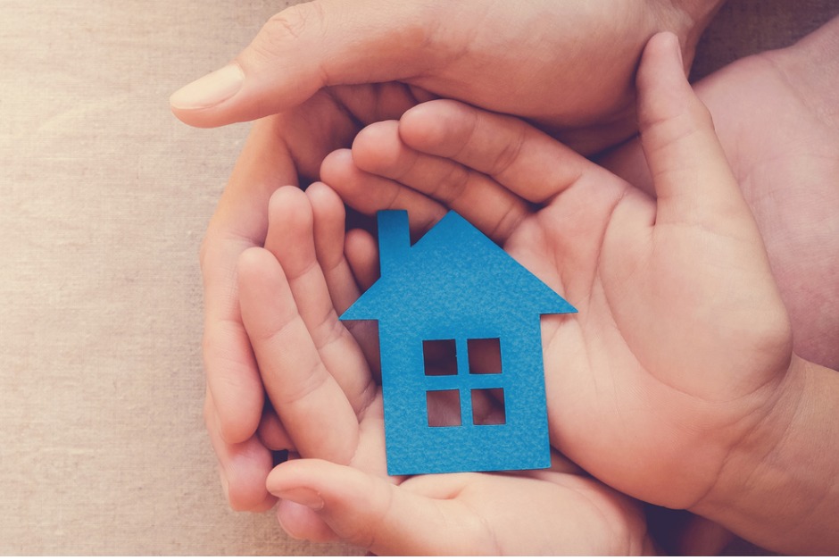 hands holding a blue house made of paper