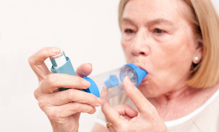 A woman holds a spacer and asthma reliver to her mouth.