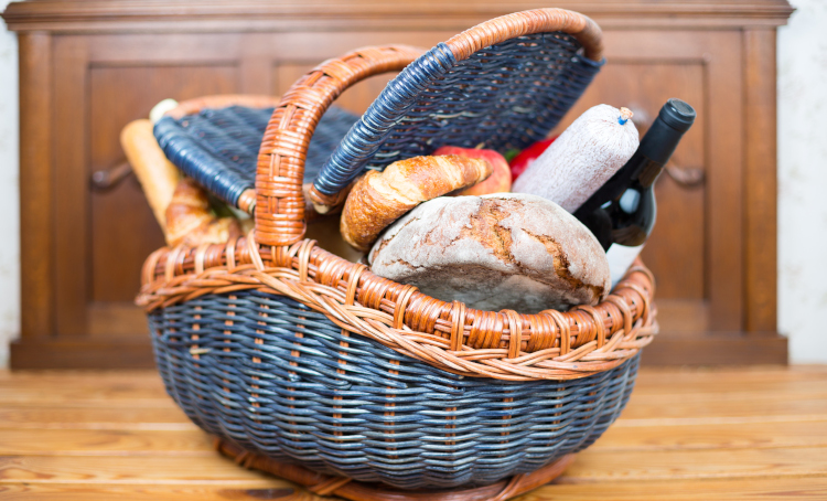 Picnic basket with croissants, a loaf of bread, apples, salami and wine