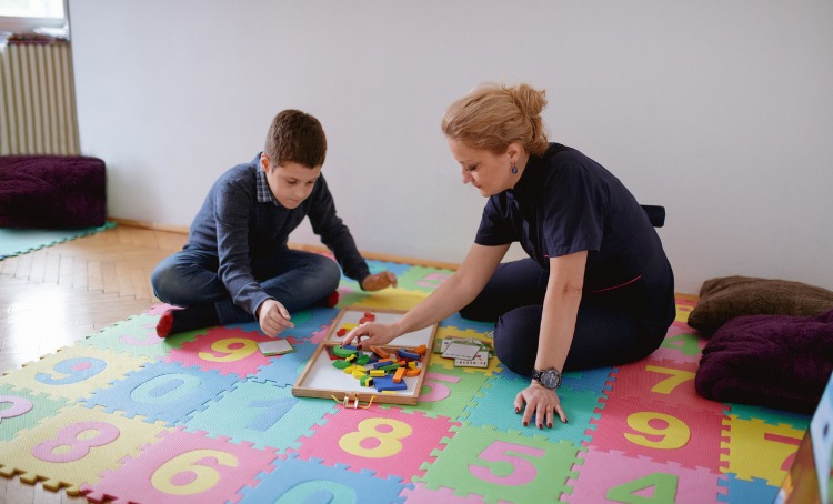 boy sitting on the floor with female tutor and working on motor skills