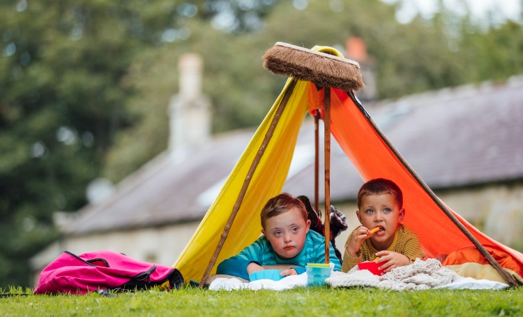 Two boys in a tent they have made with brooms, sheets and poles.