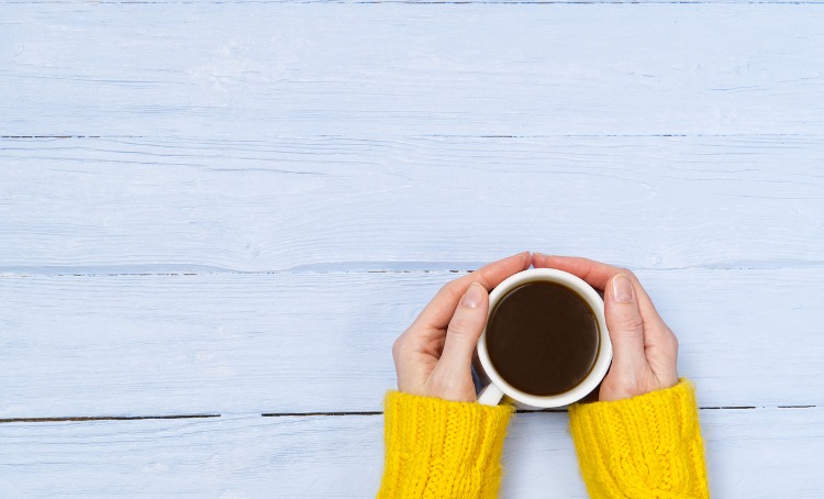 A womans hands hold a mug of warm drink.