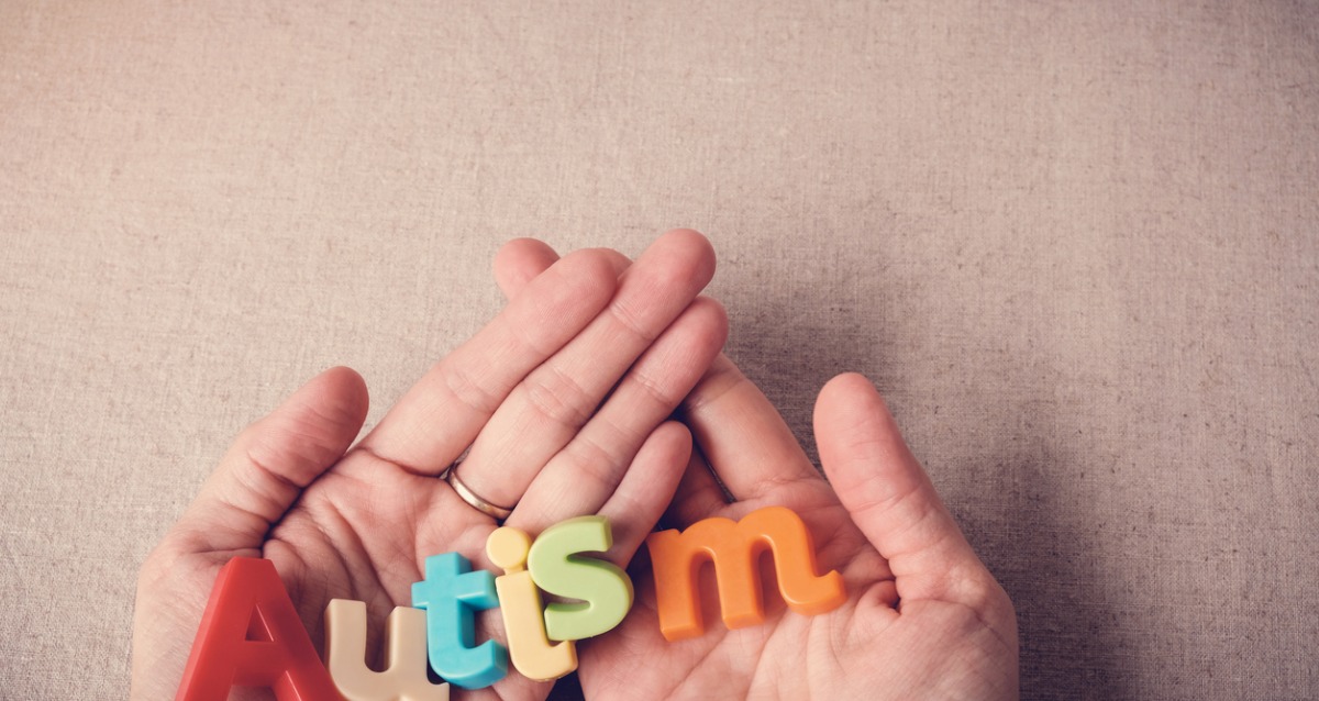  AUTISM written with colourful alphabet magnets, resting on hands