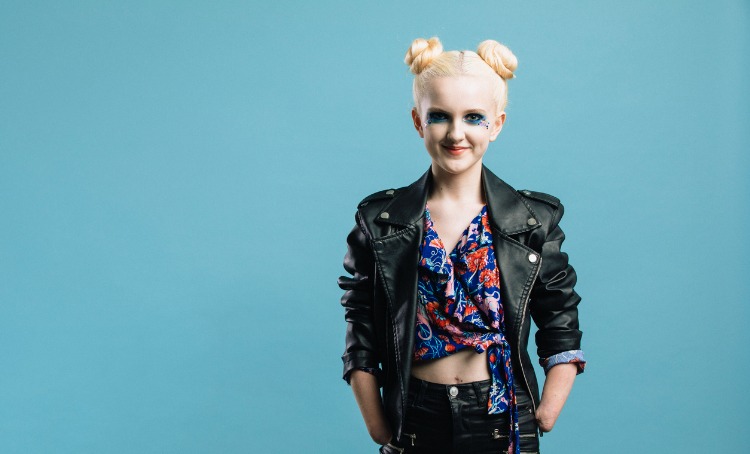 Creative photography. A girl in a black leather jacket, floral top and jeans poses for the camera. Her hair and makeup is done. She has visible disability.