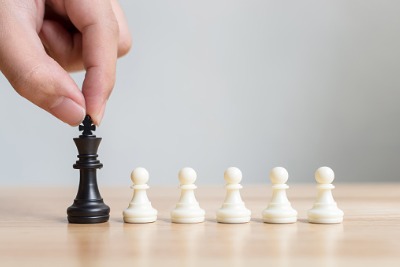 Image of hand holding black chess piece (King) with a row of white chess pieces (pawns)