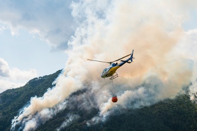 Image of a helicopter carrying a bucket of water near a bushfire.