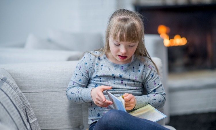 girl with down syndrome reading a book at home picture a fireplace in the background