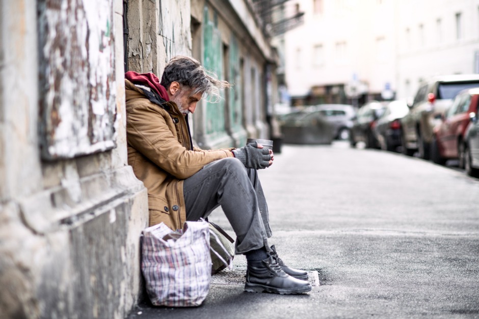 Image of homeless man sitting on a the side of a footpath.