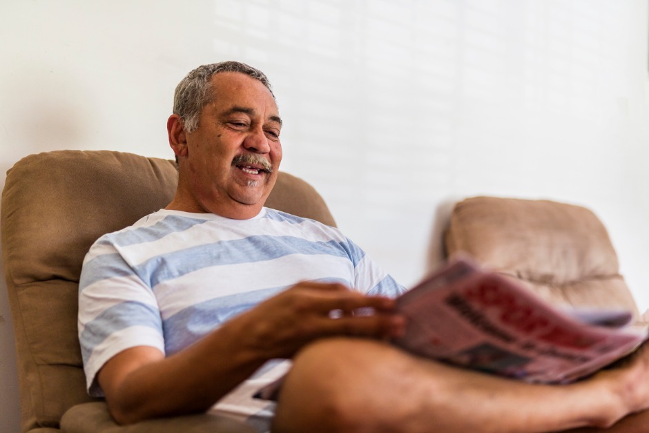 Image of smiling Aboriginal man sitting on a couch with his leg crossed.