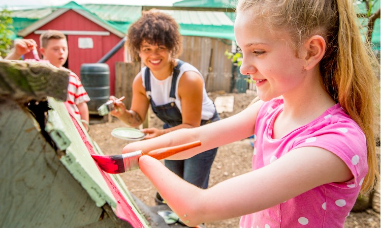 Girl with limb difference painting a chicken coop 