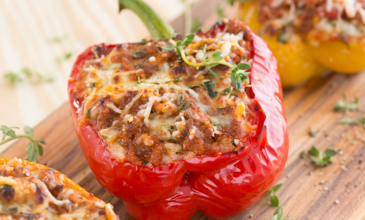 A photograph of a cooked red capsicum, the side is cut off and it is stuffed with cooked mince, melted cheese and has some herbs sprinkled on top.
