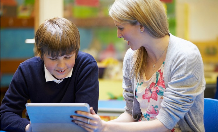 teacher with male student using digital tablet in classroom