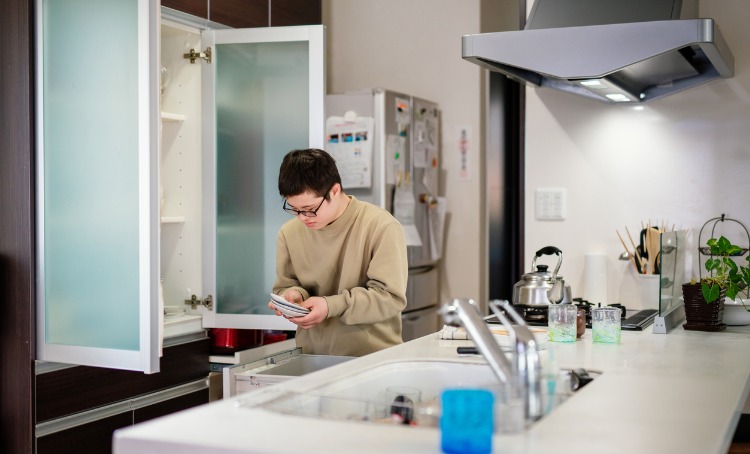 teenage boy with disability helping with house chores by putting dishes away