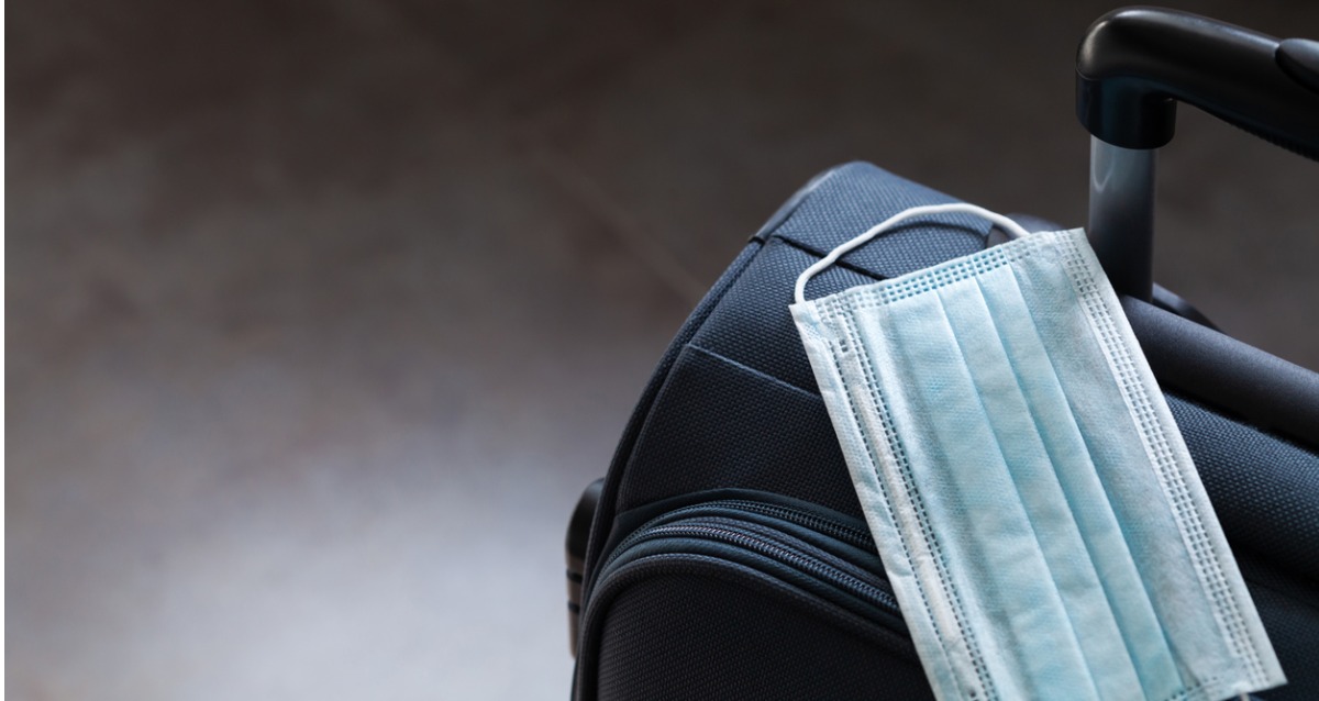 An image of a suitcase with a face mask sitting on top.