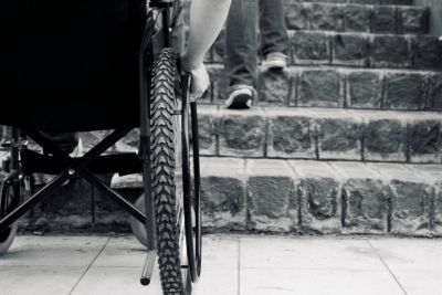 Black and white image of wheelchair in front of a flight of stairs, being unable to go up them.